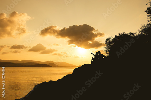 Silhouette of romance couple sitting on a rock in sunset