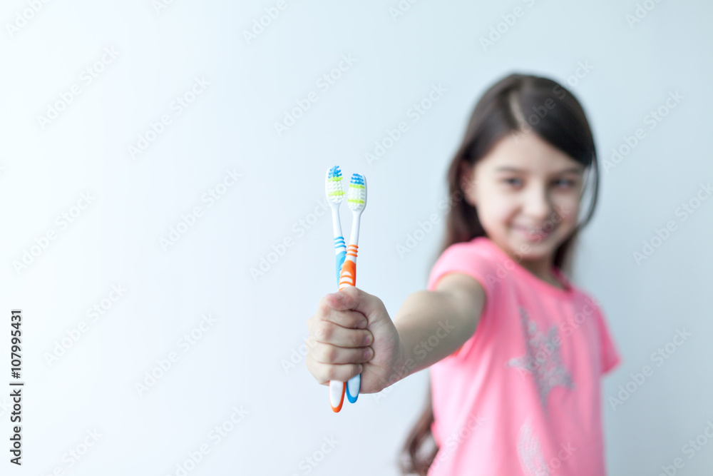 Little girl looking at the camera and smiling, holding in his outstretched hand two toothbrushes on white background Little girl looking at the camera and smiling, holding in his outstretched hand two toothbrushes on white background