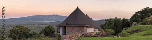 Panoramic view on lodge hotel bungalows against sunrise glowing over mountain background at dawn. Ngorongoro, Great Rift Valley, Tanzania, East Africa.
