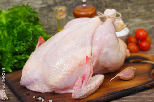 Whole raw chicken with vegetables and spices on a wooden table