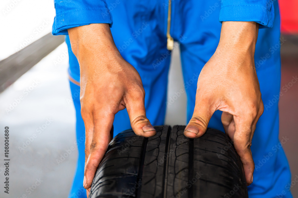 Mechanic holding and checking car wheel in car garage service