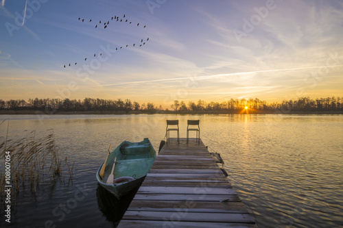 Fototapeta Naklejka Na Ścianę i Meble -  Łódka zacumowana przy drewnianym pomoście w piękny poranek nad jeziorem