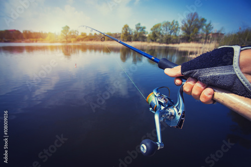 hand with spinning and reel on the evening summer lake