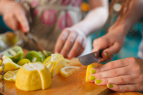 Children cooking at the kitchen. Hands cutting fresh organic lemons on the wooden table. Fruit snack. Kids making lemonade.