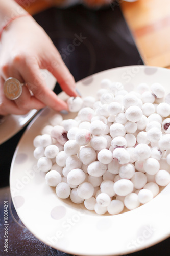 A hand with a ring taking small white sweets from the white plate. Many round candies on the big plate. Snacks for the party. Light dessert.