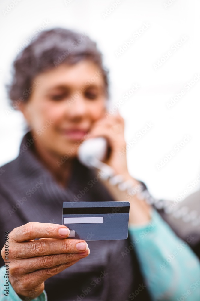 Mature woman holding payment card while talking on telephone Mature woman holding payment card while talking on telephone