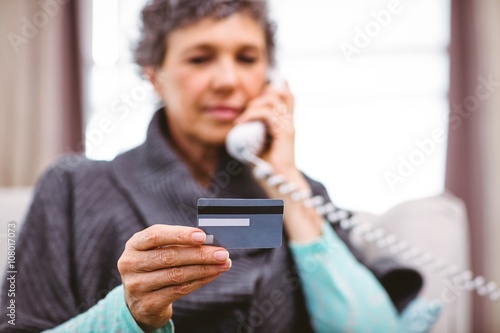 Mature woman holding credit card while talking on telephone