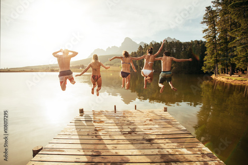 Young people jumping from pier into lake together