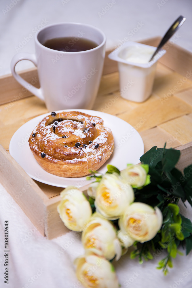 breakfast concept - close up of wooden tray with bun, tea, yoghu breakfast concept - close up of wooden tray with bun, tea, yoghu