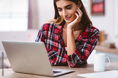 Smiling woman using laptop with hand on chin 