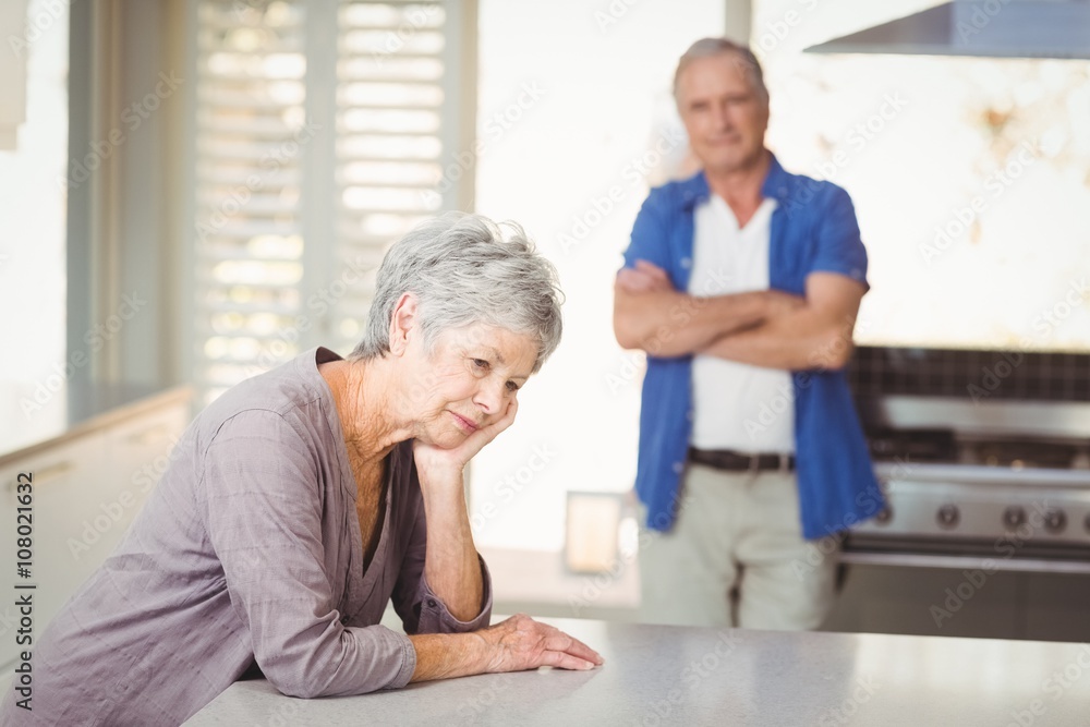 Worried senior woman sitting with man standing in background Worried senior woman sitting with man standing in background