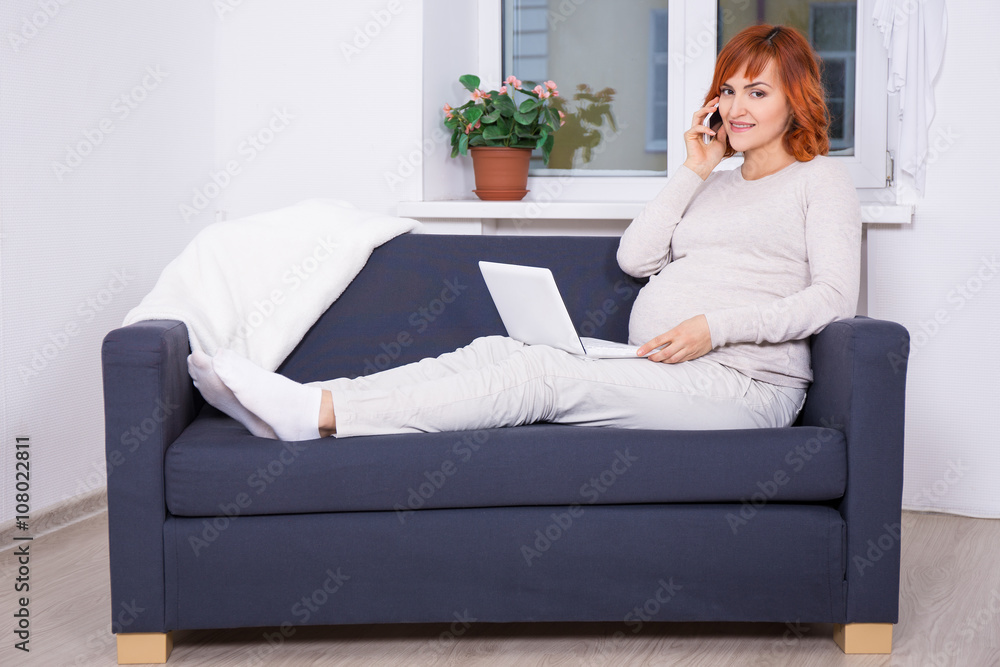 young pregnant woman using laptop and talking by phone at home young pregnant woman using laptop and talking by phone at home