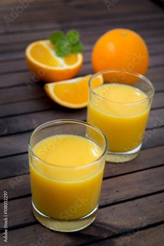 Freshly squeezed orange juice in glass, with fruits on wooden background