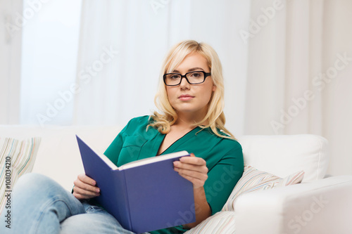 young woman in glasses reading book at home © Syda Productions