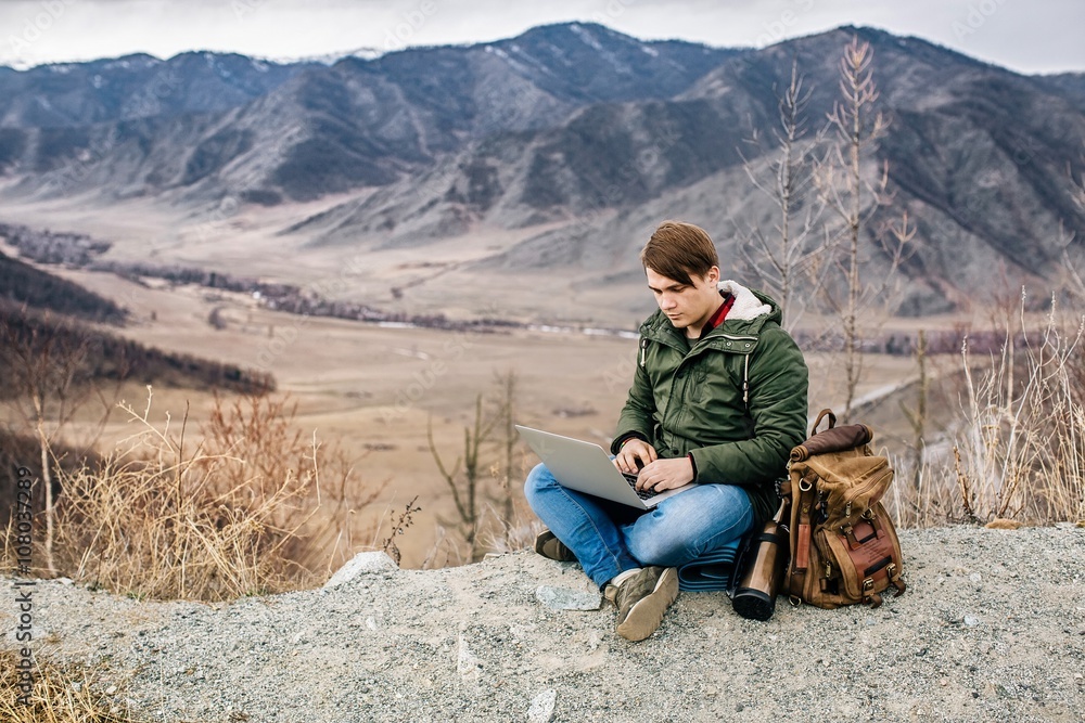 man working outdoors with laptop on the background of mountain scenery