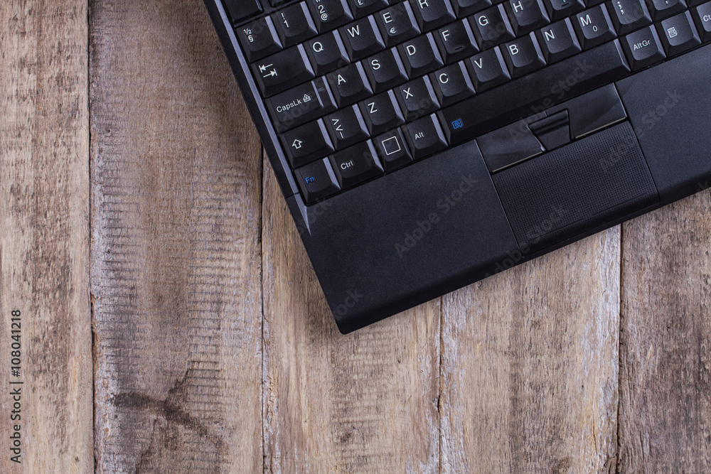 black laptop keyboard on the right on a brown wooden table - background with copyspace