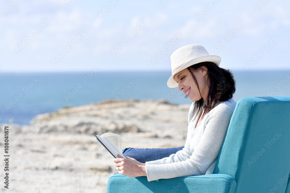 Woman reading book in armchair by the sea