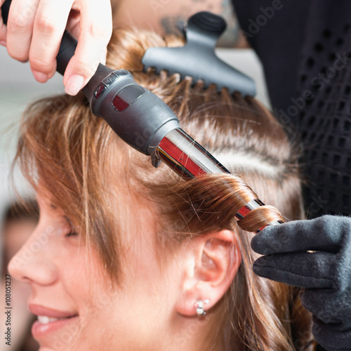 Hair salon. Hair stylist using curling tongs