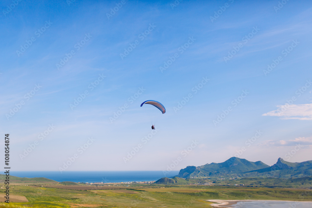 Paraglider flying against a backdrop of mountains and sea Paraglider flying against a backdrop of mountains and sea