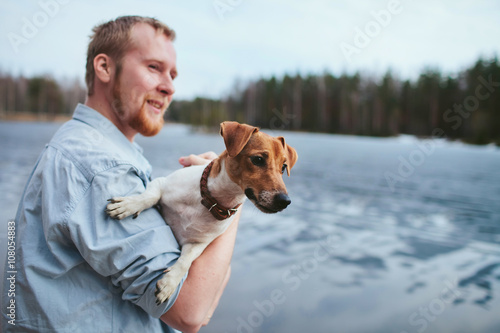 man holds a dog, standing along the shore of the lake and the forest © stock.film