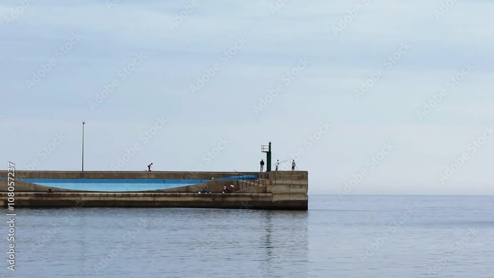 Fishermen on a concrete pier trying to catch fish. Wall built of concrete as a part of the harbor. Fishermen on a concrete pier trying to catch fish. Wall built of concrete as a part of the harbor.