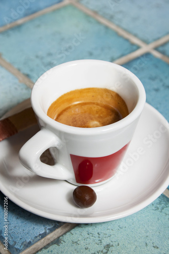 Prepared espresso coffee in a red and white cup with saucer and pralines on blue ceramic tiles.