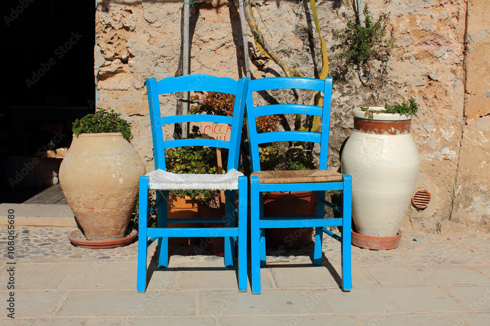 Due sedie blu al sole con due vasi grandi