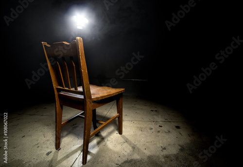Isolated wooden chair in a dark scary prison with an interrogation spotlight photo