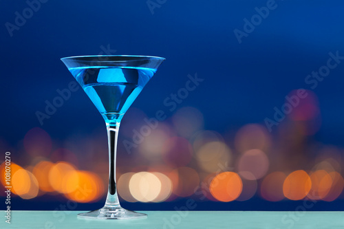 Obraz na plátně Glass of martini standing against city lights