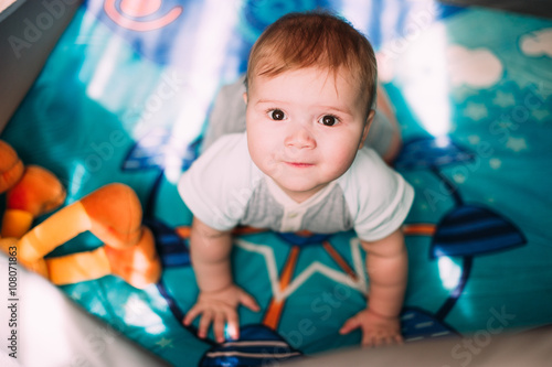 Cute little baby boy playing in colorful playpen, indoors. Beautiful child having fun at nursery.