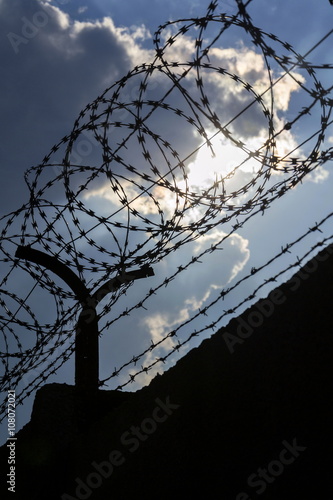 Dramatic clouds behind barbed wire fence on a prison wall