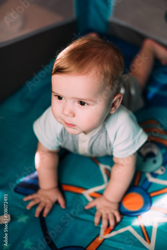 Cute little baby boy playing in colorful playpen, indoors. Beautiful child having fun at nursery.