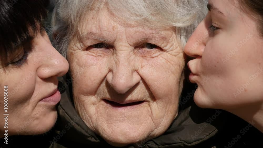 Young girl and adult woman kissing grandmother on cheeks, Granny smiling and looking to the camera. Three family generations. Grandmother, mother and granddaughter. Young girl and adult woman kissing grandmother on cheeks, Granny smiling and looking to the camera. Three family generations. Grandmother, mother and granddaughter.