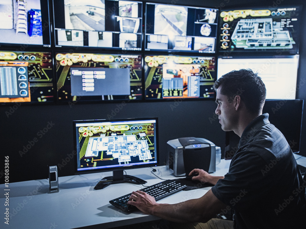 Hispanic security guard watching monitors in control room Hispanic security guard watching monitors in control room