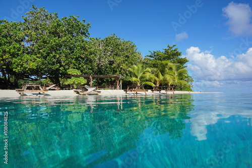Tropical beach of an islet with picnic tables on the shore, seen from water surface, Huahine island, French Polynesia