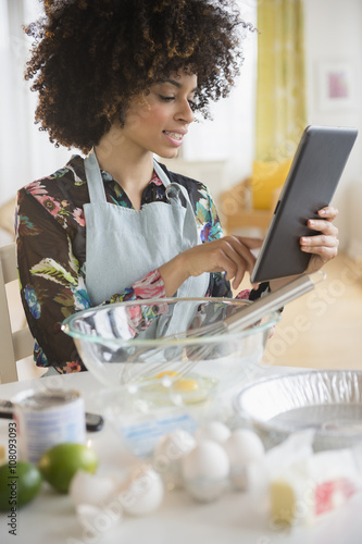 Mixed race woman baking with recipe on digital tablet photo