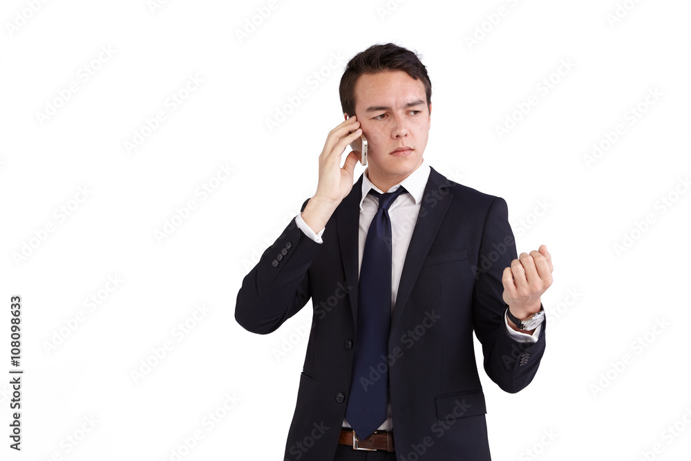 A young caucasian male businessman frowns with raised hand while holding a mobile phone looking away from camera. A young caucasian male businessman frowns with raised hand while holding a mobile phone looking away from camera.