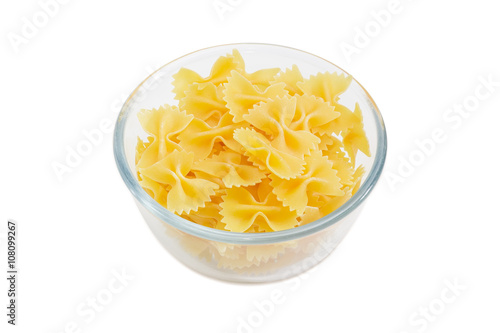 Uncooked bow-tie pasta in glass bowl on light background photo