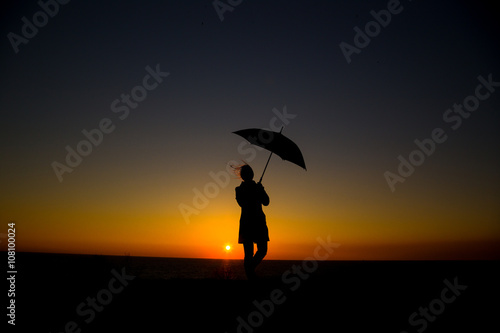 Woman holding and umbrella in silhouette against orange sunset