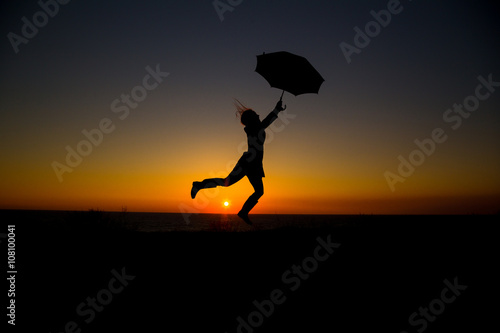 Woman holding and umbrella in silhouette against  orange sunset