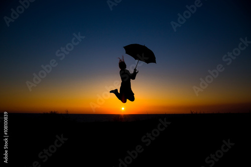Woman holding and umbrella in silhouette against orange sunset