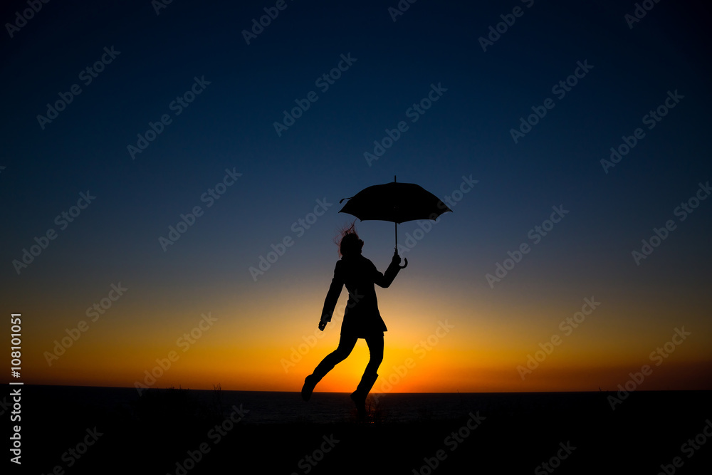 Woman holding and umbrella in silhouette against  orange sunset