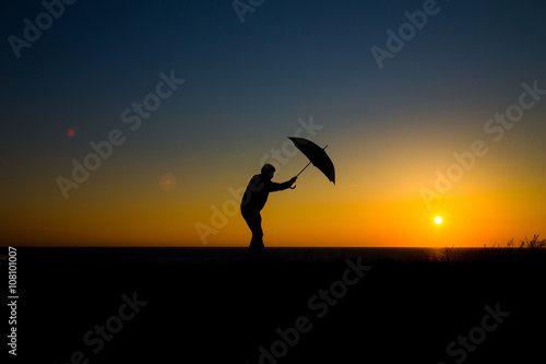 Man holding and umbrella in silhouette against orange sunset