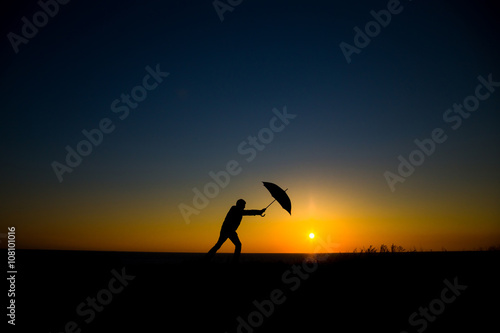 Man holding and umbrella in silhouette against orange sunset