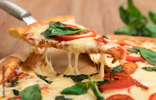Pizza Margherita with tomatoes, mozzarella and basil on a wooden background, a slice of pizza with cheese stretching, close-up