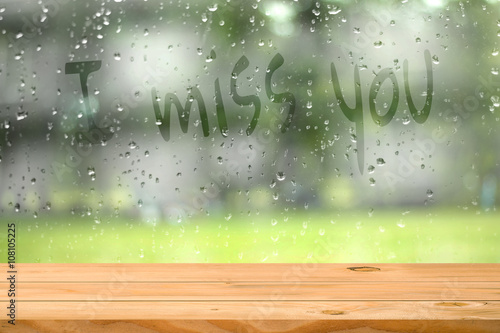 Картината върху платно Empty wooden table near water drop on window with wording i miss you blurred garden background
