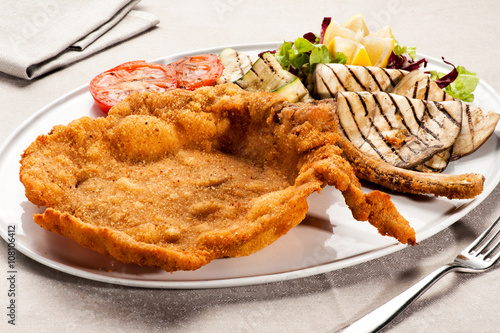 Fototapeta Fried Milanese cotoletta with tomatoes on plate