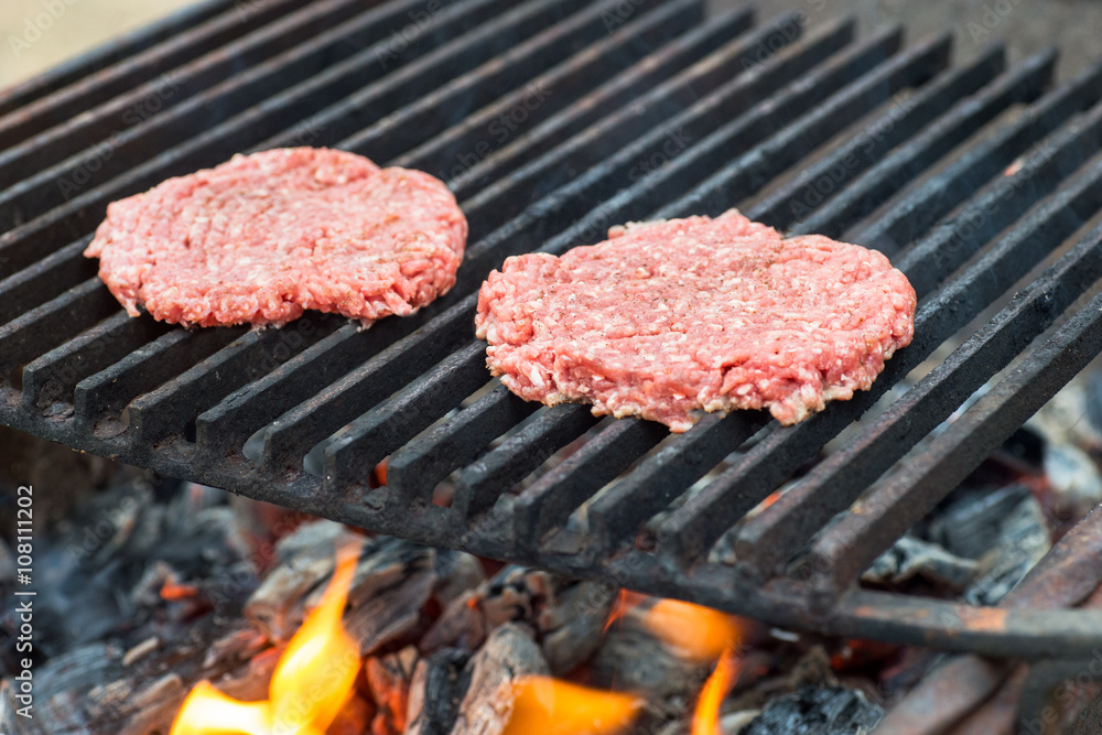 Two raw hamburger slices cooking on grill with flames
