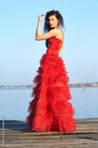 Charming female model wearing magic red dress at the lake pier outdoor portrait © sebastiangora