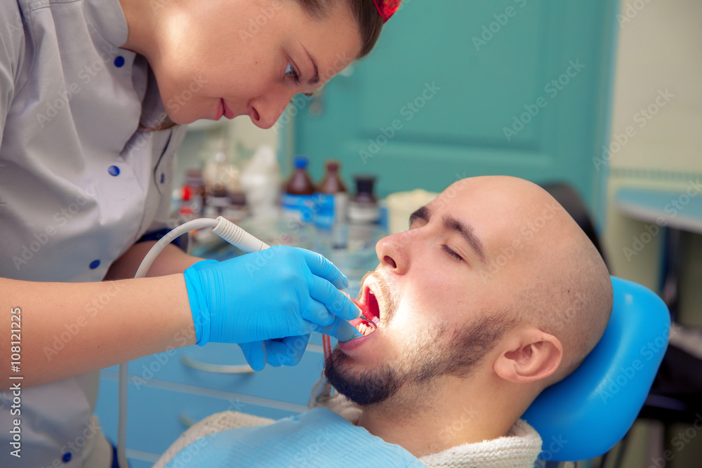 handsome guy treats caries teeth in the dental office